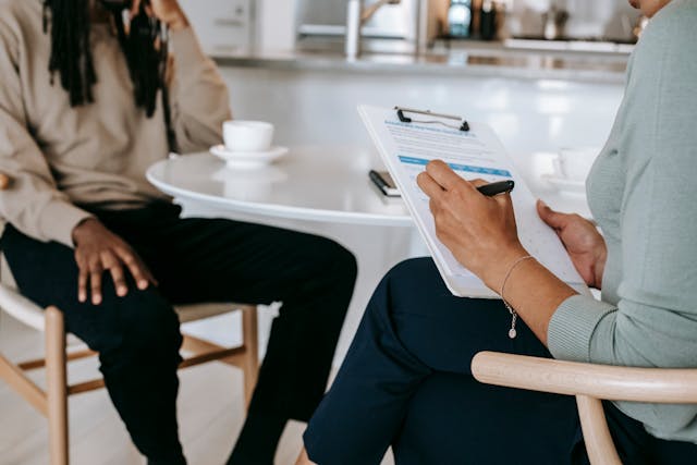 two people sitting at a white round table while one checks off things on a piece of paper