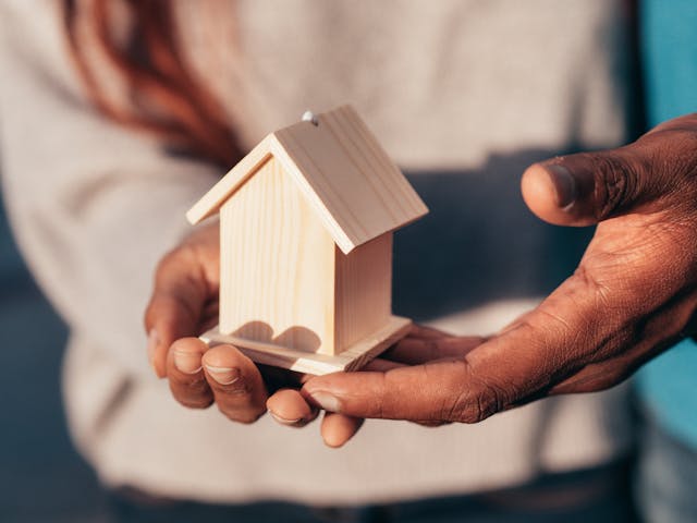 two people holding a miniature wooden carving of a home